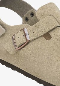 Sandalo in suede beige chiaro con strap a fibbia e design con fori. Presenta una finitura testurizzata e una suola in gomma scura.