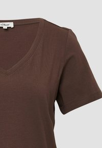 Bruine V-hals T-shirt met korte mouwen, gemaakt van zacht, geribbeld materiaal. heeft een label op de halslijn. Eenvoudig, casual ontwerp.