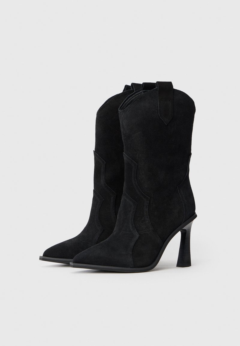 Stivaletti neri in suede, con punta affusolata, cuciture arcuate e tacco a stiletto di 3 pollici. Presentano linguette per facilitare l'indossamento.