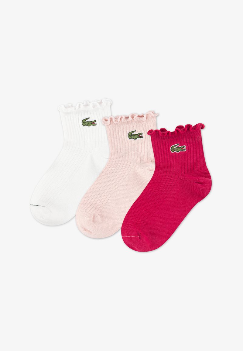Trois paires de chaussettes côtelées en blanc, rose clair et rose foncé, avec un bord à volants et un petit logo crocodile vert.