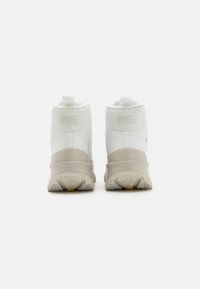 Sapatilhas Nike de cano alto em couro branco com uma sola beige suave. Apresentam uma sola texturizada para aderência e uma marcação discreta no calcanhar.