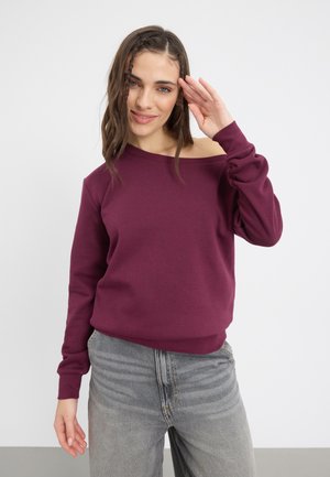 Burgunderfarget off-shoulder genser med myk tekstur, lange ermer og avslappet passform, kombinert med løse grå jeans. Minimalistisk design.