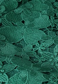 Emerald green embroidered fabric featuring floral patterns and intricate stitch detailing, giving a textured and dimensional appearance.