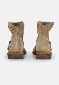 Botines de ante en un tono beige claro, con detalles de corte en la parte trasera, un tacón de madera apilada y una suela de goma plana.