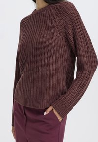 Strickpullover in Burgunderrot mit strukturiertem Muster, Rundhalsausschnitt und gerippten Bündchen. Kombiniert mit passenden Hosen in lässigem Schnitt.