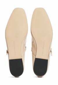 Le scarpe da donna Tommy Hilfiger presentano una tomaia in materiale sintetico beige liscio, una sottile fascia e una presa nera sulle suole, con un dettaglio del logo in rilievo.