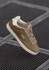 Brown suede sneaker with cream accents, round toe, and perforated detailing. Features Fila logo and rubber outsole for traction.