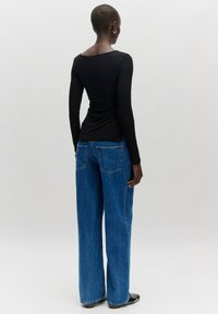 Schwarzes langärmliges Oberteil, tailliert geschnitten. Hellblaue weite Jeans mit zwei Gesäßtaschen und einer leichten Denim-Textur. Minimalistisches Design.