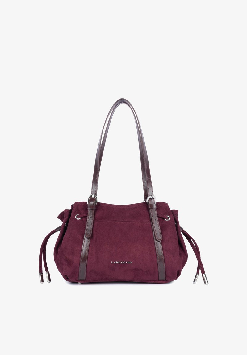 Sac à main en daim rouge foncé avec deux lanières en cuir marron foncé, boucles argentées, liens latéraux et le nom de la marque "Lancaster" sur le devant.