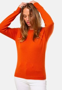 Pull en tricot orange à manches longues, décolleté rond et ourlet côtelé. Le tissu semble doux et extensible, assorti à un pantalon blanc.