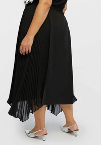 Jupe midi plissée noire avec un ourlet fluide, fabriquée en matériau léger ; associée à des chaussures à talons argentées, mettant en valeur un design élégant.