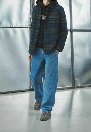 Plaid jacket in dark blue and green over a black hoodie, paired with light blue wide-leg jeans and gray sneakers. Smooth texture, casual fit.