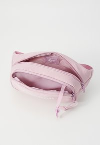 Pochette en tissu rose avec fermeture éclair, dotée d'une poche intérieure et d'une étiquette logo. Texture lisse et bords arrondis.