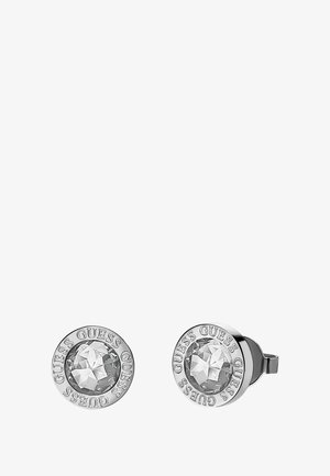 Silver stud earrings featuring a clear, faceted crystal center, surrounded by an embossed circular border with "GUESS" lettering.