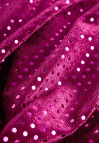 Fuchsiahäftad tyg med en texturerad yta, som har blanka cirkulära paljetter och jämnt fördelade hål, vilket skapar ett mönstrat utseende.