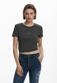 Dark gray cropped t-shirt with a round neckline and short sleeves, featuring an embossed "DSGL" logo on the front. Paired with high-waisted blue jeans.