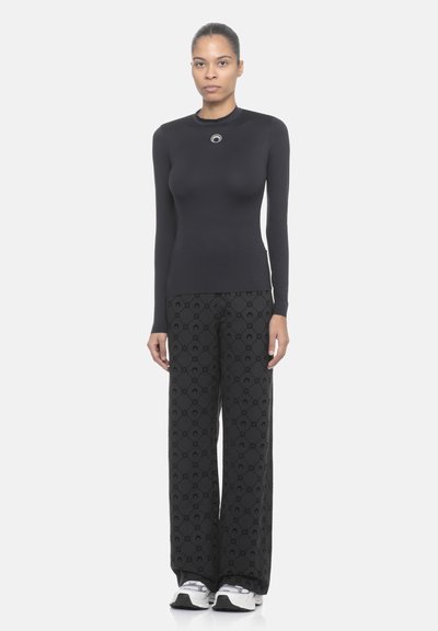 Maglia nera a maniche lunghe con scollatura rotonda e dettagli argentati, abbinata a pantaloni neri larghi con un motivo sottile e scarpe da ginnastica.