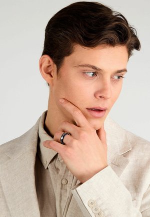 Heren lichtbeige linnen blazer over een bijpassend overhemd met knopen, en een donkere bandring met metalen accenten op de hand.