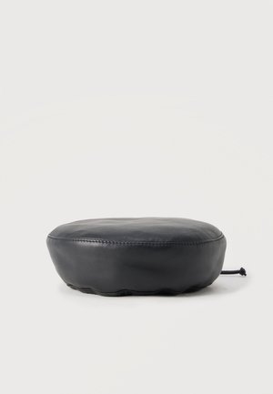 Coussin rond en cuir noir avec des coutures visibles et un cordon de serrage sur un côté, placé sur un fond clair uni.