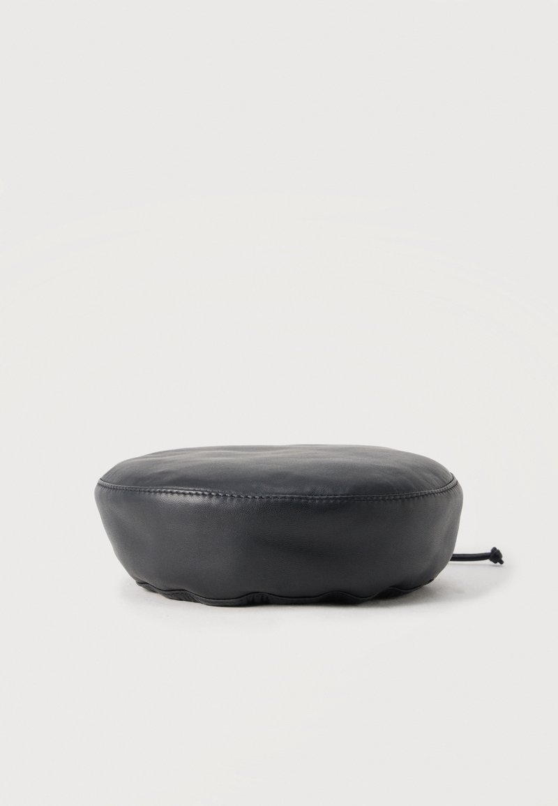 Μαύρο στρογγυλό μαξιλάρι από δερματίνη με ορατή ραφή και κορδόνι σε μία πλευρά, τοποθετημένο σε απλό ανοιχτό φόντο.