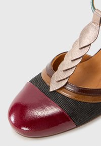 Burgundy and black leather shoe with a glossy toe cap, textured mesh body, and a braided metallic strap. Round toe design.