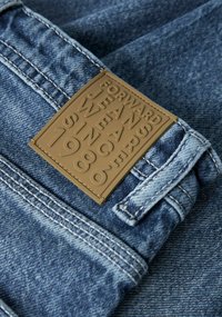 Jeans in denim con un'etichetta in pelle marrone testurizzata con testo in rilievo "FORWARD JEANS WE ARE SINCE 1986" cucita in vita.