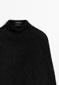 Maglione a collo alto in cashmere nero con una consistenza morbida e soffice e un collo alto; etichette visibili indicano la composizione del tessuto e l'origine.