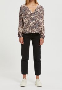 Långärmad blus i ett flerfärgat, abstrakt mönster med V-ringning, kombinerad med svarta avklippta jeans och vita sneakers.