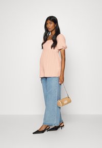 Top pêssego com nervuras e mangas bufantes, combinado com jeans de perna larga azul-claro. Acessórios incluem uma mala cilíndrica bege e sapatos pretos de bico fino.
