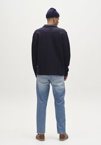 Tengerészkék kötött dzseki gallérral, laza szabású, világoskék farmernadrággal párosítva. Barna bőrcipők teszik teljessé az öltözetet. Egyszerű design, minták nélkül.