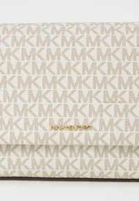 Geantă de mână de culoare crem, prezentând un model texturat cu logo-uri interconectate „MK”. Accentele din metal auriu afișează logo-ul „MICHAEL KORS”.