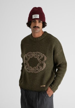 Knit sweater in dark green with a large beige circular pattern at the center. Features ribbed crew neck and frayed hem detail.