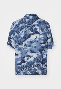 Camicia a maniche corte in tessuto blu con stampa tropicale raffigurante palme e barche a vela, accentuata dal testo "Tommy Jeans" in bianco.