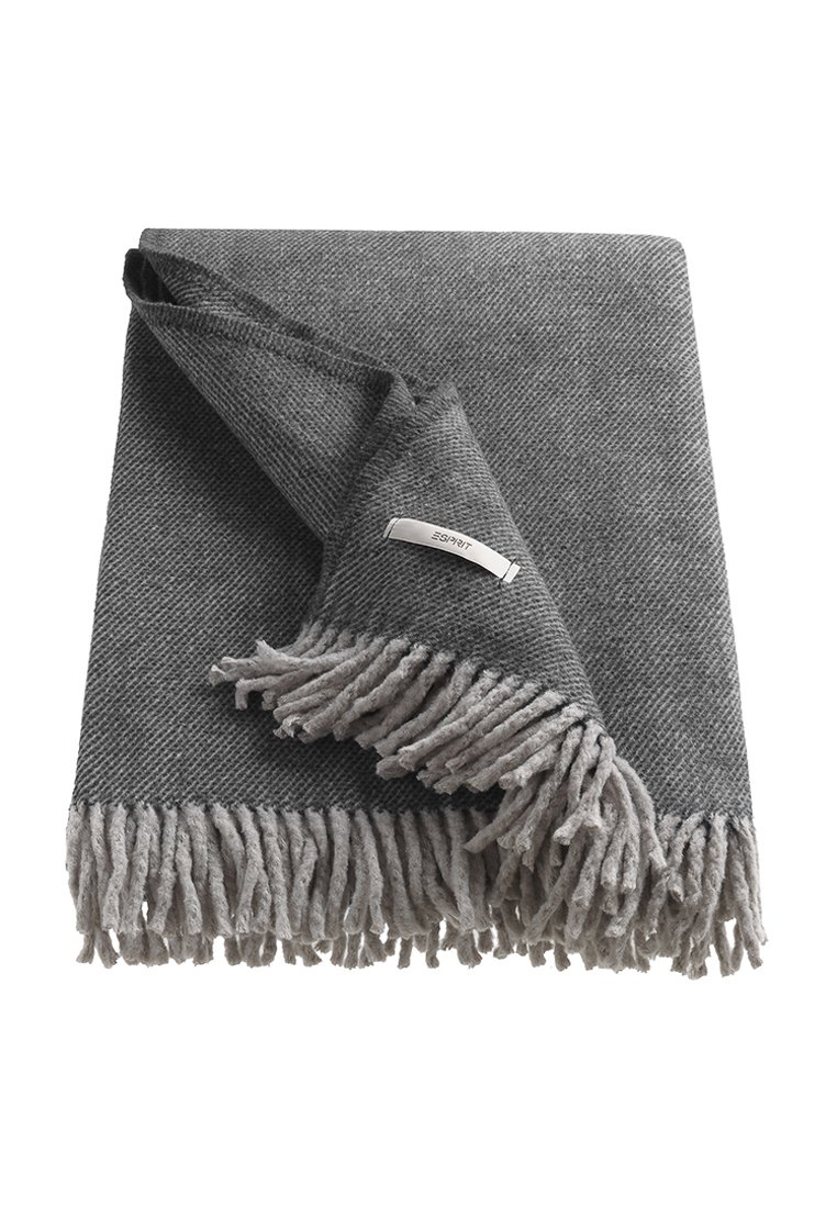 Manta de tejido gris con patrón de espiga texturizado, bordes con flecos en gris claro, que presenta una pequeña etiqueta de metal con el nombre de la marca.