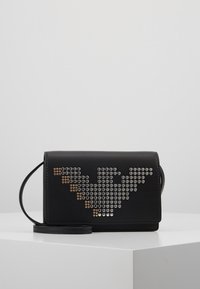 Černá obdélníková crossbody taška se stříbrnými a zlatými kulatými hroty vytvářejícími geometrický vzor ve tvaru V na předním klopu.