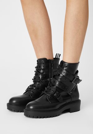 Black leather ankle boots with strap and stud details, featuring a side zipper and rugged sole for traction. Textured finish adds durability.