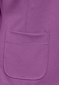 Purple fabric featuring a patch pocket with a rounded edge, seamless texture, and visible stitching details. Simple, functional design.