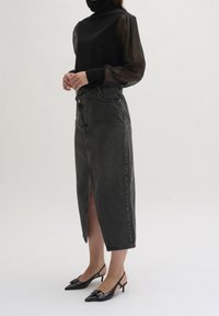 Svart polotröja med genomskinliga ärmar, i kombination med en högmidjad, knälång grå jeanskjol med en framficka, och svarta slingback-höga klackar.