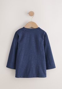 Mörkblå långärmad skjorta i mjukt tyg, med ribbad krage och enkel design, upphängd på en trägalge mot en ljus bakgrund.