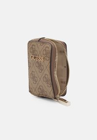 Hnědá peněženka se vzorem a zlatým zipem, na přední straně s logem "GUESS". Materiál má texturovaný bavlněný povrch.