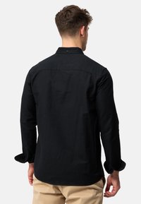 Chemise noire à manches longues avec col boutonné. En tissu robuste, dotée d'une coupe droite et de manches retroussées. Design minimaliste.