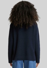 Pull en maille côtelée marine à manches longues, offrant une coupe décontractée et une finition texturée. L'ourlet est légèrement plus long à l'arrière.