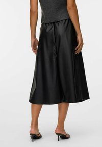 Zwarte midi-rok van glad nepleer, met een flared ontwerp en een elastische tailleband, gedragen met zwarte hoge hakken.