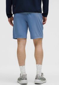 Lyseblå sportsbukser med en glat tekstur, i midt-lår længde, kombineret med grå sneakers og hvide sokker. Baggridsvinkel af outfittet.
