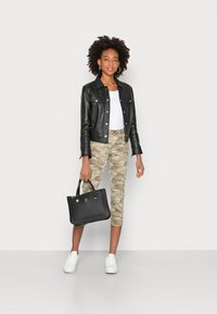 Jaqueta de couro preta sobre uma blusa branca, combinada com calças com padrão de camuflagem e ténis brancos. Uma bolsa preta é segurada em uma mão.