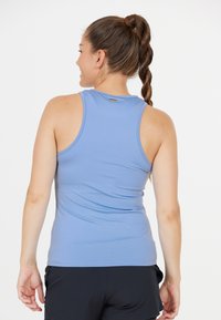 Valkoinen vaaleansininen tanktoppi, jossa on sileä pinta, jossa on urheilullinen selkädesign ja pieni logo korostus yläselässä. Yhdistetty mustiin shortseihin.