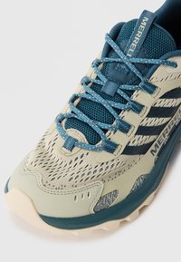 Jasnoszare i tealowe buty sportowe z siateczkową cholewką, wzmocnionym czubkiem i teksturowaną podeszwą. Posiadają niebieskie sznurówki i oznakowanie z boku.