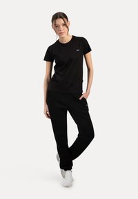 Sort bomulds T-shirt med rund hals og lille logo, parret med løse sorte sweatpants. Modellen har hvide sneakers på.