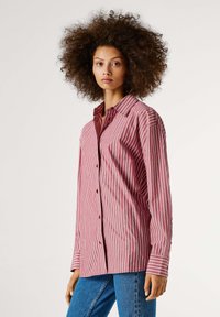 Camisa de botones a rayas rojas y blancas con mangas largas y collar clásico, hecha de una tela ligera. Presenta un corte relajado.