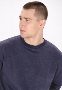 Sudadera a giro navy con maniche lunghe e tessuto testurizzato. Il collo è rinforzato con un bordo a coste, conferendo un aspetto strutturato.
